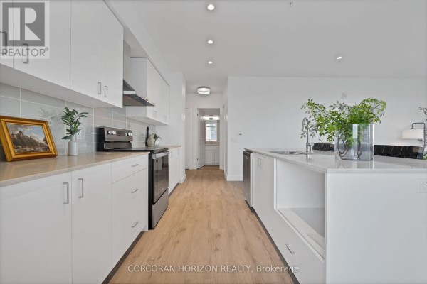Galley kitchen with white cabinets and island, leading to a hallway. - 1702 - 50 Grand Avenue S, Cambridge