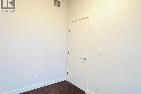 Empty room with white walls, white door, and dark wood floors. - 1702 567 Clarke Road, Coquitlam