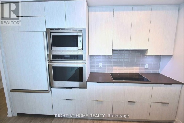 Built-in stainless steel microwave and oven above integrated refrigerator and white cabinetry in the kitchen. - 1703 - 56 Annie Craig Drive, Toronto