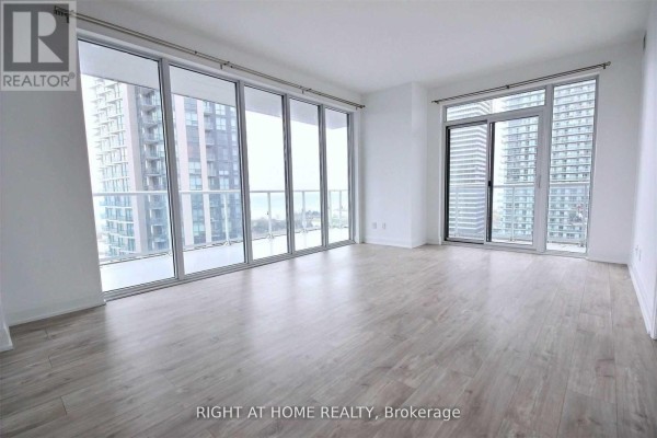 Spacious, empty living room with light wood floors and large windows offering city views. - 1703 - 56 Annie Craig Drive, Toronto