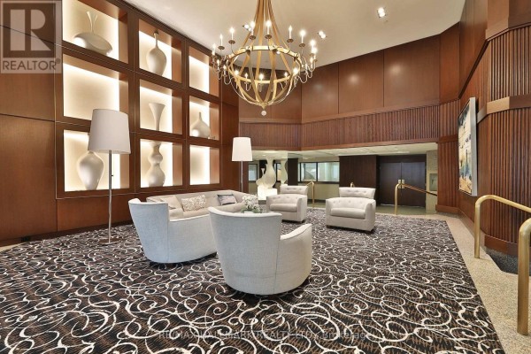 Lobby seating area featuring light gray upholstered furniture, a patterned carpet, and a large chandelier. - 1704 - 10 Kenneth Avenue, Toronto