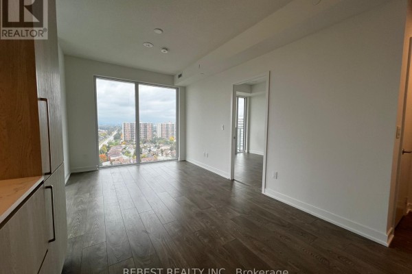 Living area with large windows, dark wood floors, and a doorway leading to another room. - 1704 - 209 Steeles Avenue W, Brampton
