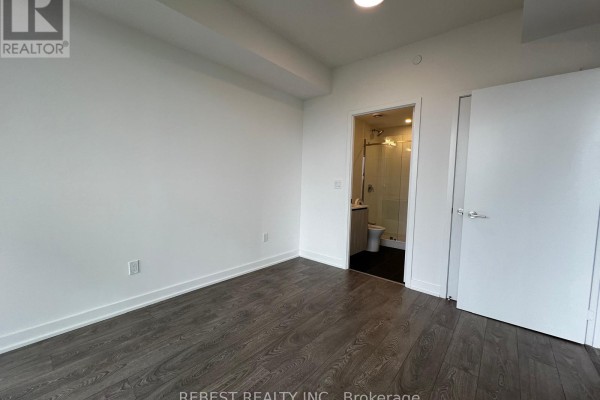 Bedroom with doorway to bathroom, white walls, and dark wood floors. - 1704 - 209 Steeles Avenue W, Brampton