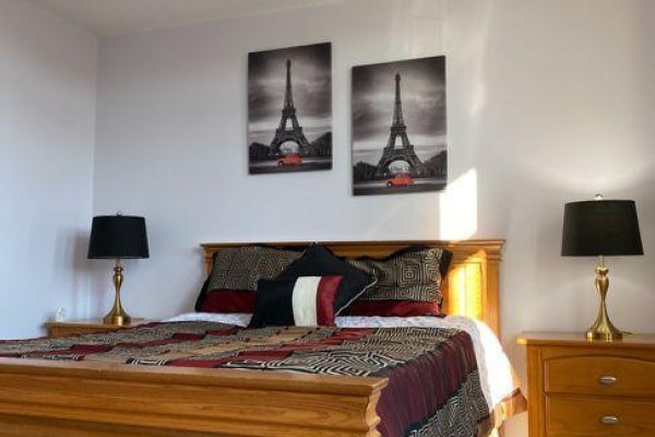 Bedroom with a wooden bed frame, patterned bedding, and Eiffel Tower wall art. - 1704 - 530 Lolita Gardens, Mississauga