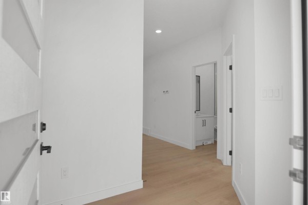 Entrance hallway with white walls, light wood flooring, and a view into a bathroom. - 17040 47 St Nw, Edmonton