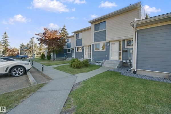 Street view of townhouses with blue and tan siding, a parked car and trees. - 17041 100 St Nw, Edmonton