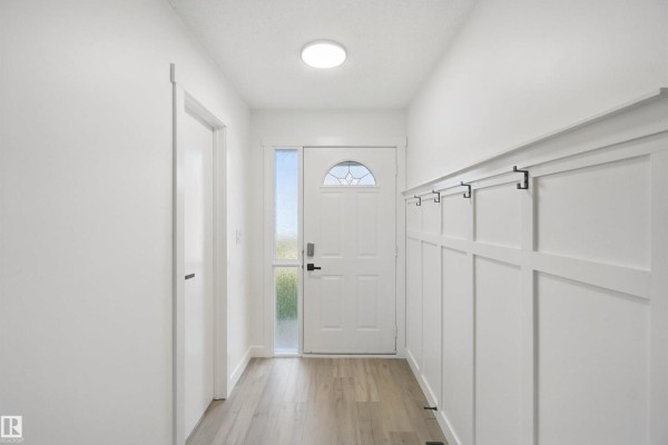 Interior entryway with white walls, wood-look flooring, and a white paneled accent wall. - 17041 100 St Nw, Edmonton