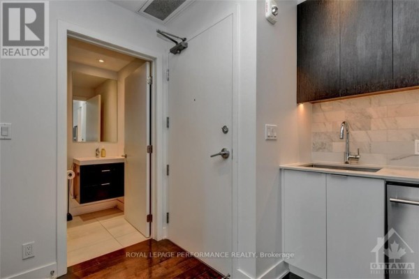 View of the apartment's entryway, showing a white door, dark wood cabinets, and bathroom entrance. - 1705 - 20 Daly Avenue, Ottawa