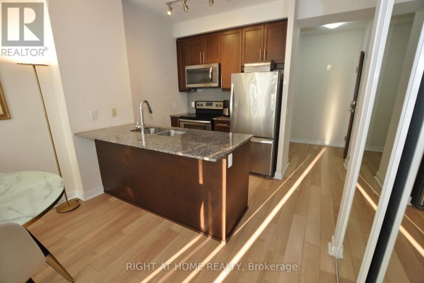 Apartment kitchen with granite island, stainless steel appliances, and light wood floors. - 1705 - 3975 Grand Park Drive, Mississauga