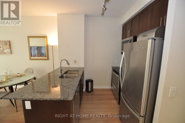 Kitchen area with dark wood cabinets, stainless steel refrigerator, and granite countertop island. - 1705 - 3975 Grand Park Drive, Mississauga