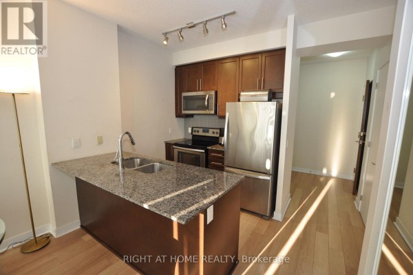 View of an apartment kitchen with dark cabinets, stainless steel appliances, and light wood flooring. - 1705 - 3975 Grand Park Drive, Mississauga