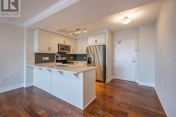 Open-concept kitchen featuring white cabinetry, stainless steel appliances, and hardwood flooring. - 1705 - 505 Talbot Street, London East