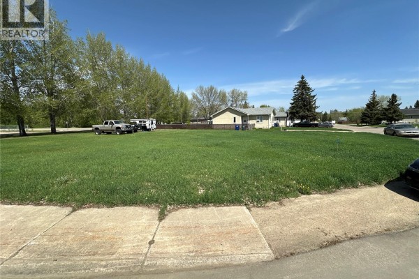 Snow-covered undeveloped land with trees and houses in the distance under a blue sky. - 1705 1st Avenue, Rosthern