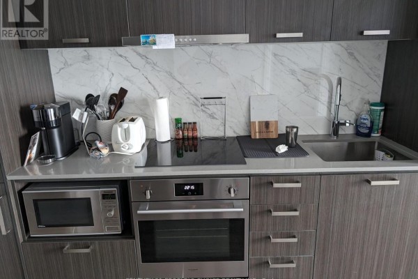 Modern apartment kitchen with dark grey cabinets, stainless steel appliances, and marble backsplash. - 1706 - 38 Honeycrisp Crescent, Vaughan