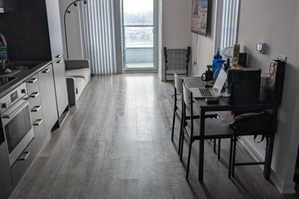 Apartment living area with grey flooring, sofa, dining table, and large window. - 1706 - 38 Honeycrisp Crescent, Vaughan
