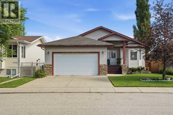 A beige house with a white garage door, red trim, and stone accents on the lower exterior. - 1706 3 Avenue Se, High River