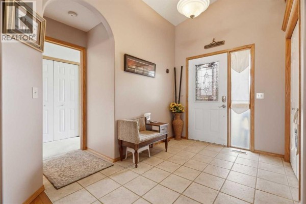 Interior entryway with beige walls, tiled floor, a bench, and a view into a hallway closet. - 1706 3 Avenue Se, High River