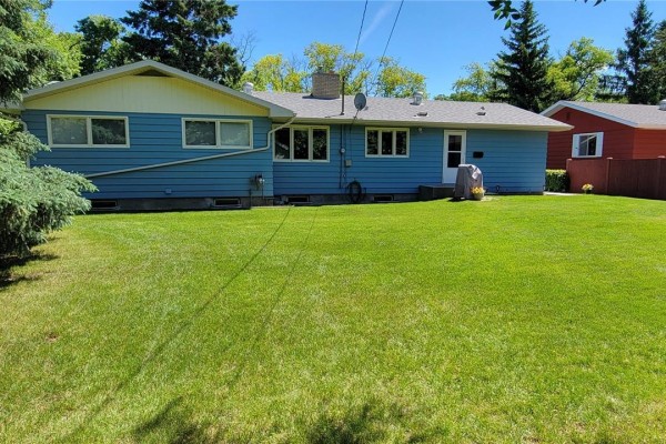 View of the rear of the house with blue siding, white trim, and windows. Green lawn in front. - 1707 98th Street, Tisdale