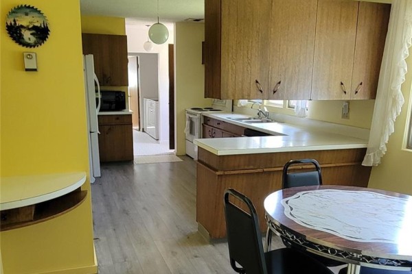 Kitchen with light yellow walls, wood cabinets, white countertops, and a round dining table. - 1707 98th Street, Tisdale