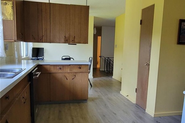 Kitchen with wood cabinets, stainless steel sink, and view of hallway and staircase to the left. - 1707 98th Street, Tisdale