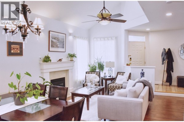 Living room with vaulted ceiling, fireplace, and large windows, featuring plants and furniture. - 1707 Arbutus Place, Coquitlam