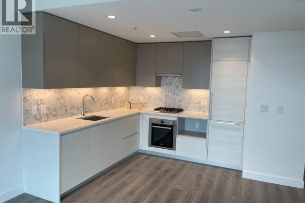Modern L-shaped kitchen with grey and white cabinetry, quartz countertops, and stainless steel appliances. - 1708 8188 Fraser St, Vancouver