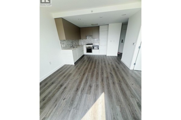View of the kitchen and living area with dark grey wood-look flooring and white walls. - 1708 8188 Fraser St, Vancouver