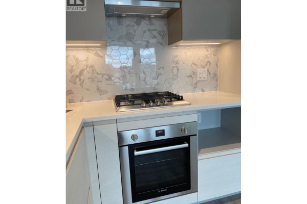 Close-up of a stainless steel gas range and oven with decorative tile backsplash in a modern kitchen. - 1708 8188 Fraser St, Vancouver