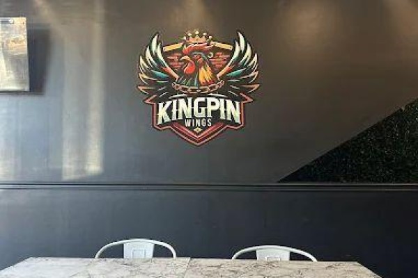 Black wall with a large, colorful 'Kingpin Wings' logo featuring a crowned rooster. - 1708 Eglinton Avenue W, Toronto