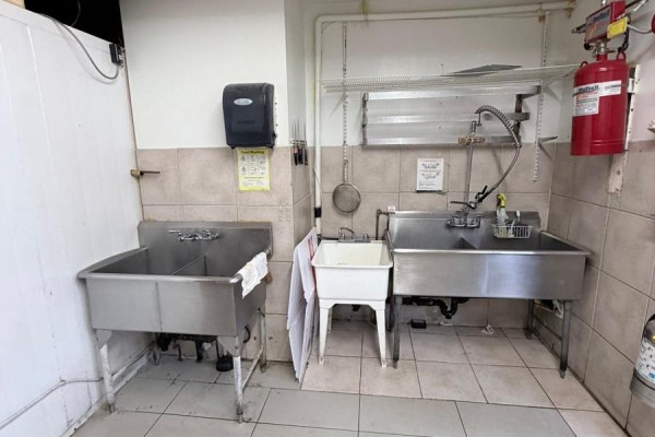 Commercial kitchen area with two stainless steel sinks and a red fire extinguisher. - 1708 Eglinton Avenue W, Toronto