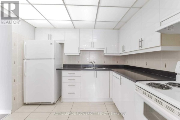 Bright white kitchen with black countertops, white appliances including a refrigerator and stove, and tiled floor. - 1709 - 115 Hillcrest Avenue, Mississauga