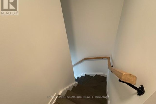 View looking down a narrow staircase with dark treads and a wooden handrail. - 171 - 1610 Charles Street, Whitby