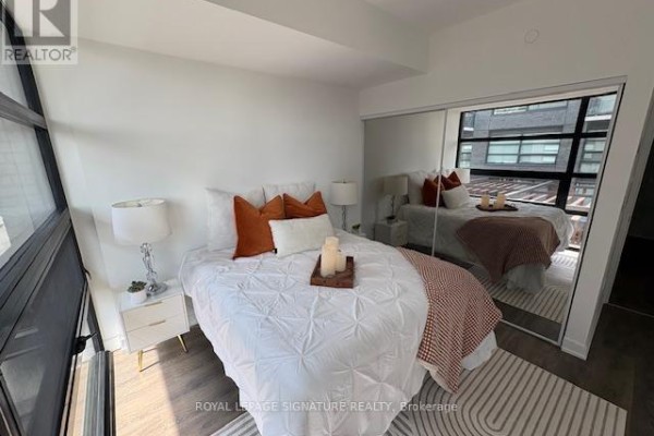 Bedroom with mirrored closet doors reflecting the bed and large windows with city views. - 171 - 1610 Charles Street, Whitby
