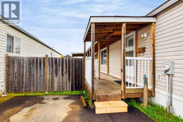 Wooden covered porch with white railings and steps leading to the entrance of the mobile home. - 171 Grant Way, Fort Mcmurray