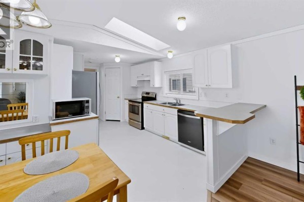 Kitchen and dining area with white cabinets, wood table, stainless steel appliances, and wood-look flooring. - 171 Grant Way, Fort Mcmurray