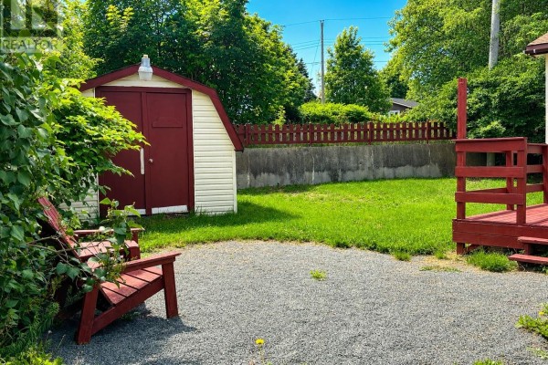 A backyard view with a gravel patio, red Adirondack chairs, a shed, and a red-railed deck. - 171 Harvey Street, Harbour Grace