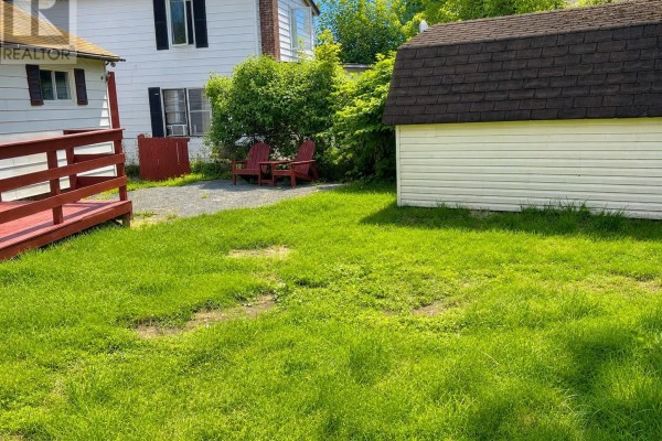 A grassy backyard with a shed, a deck, and lawn chairs, next to a white vinyl-sided building. - 171 Harvey Street, Harbour Grace