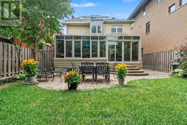 Backyard patio with a dining set and chairs, surrounded by green grass and a wooden fence. - 171 Powell Avenue, Ottawa