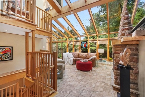 Sunroom with a leather sofa, stone fireplace, and wooden beams supporting a glass ceiling. - 171 Powell Avenue, Ottawa