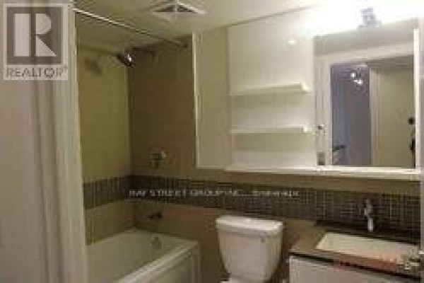 A bathroom with a white bathtub, toilet, and vanity with a large mirrored cabinet. - 1710 - 295 Adelaide Street W, Toronto