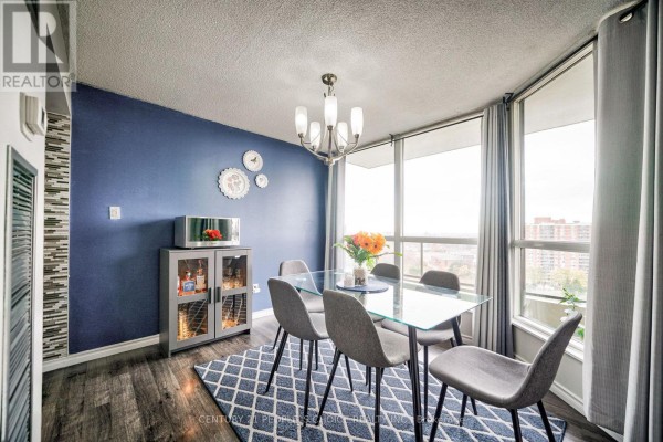 Dining area with a glass table, grey chairs, a blue accent wall, and large windows with city views. - 1710 - 5 Rowntree Road, Toronto