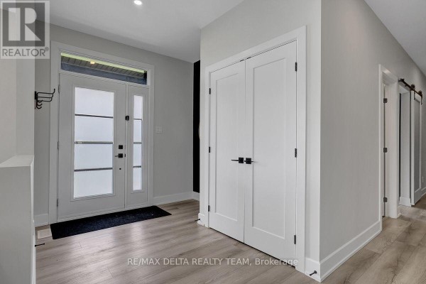 Interior entryway with light wood laminate flooring, a white double door closet, and a frosted glass front door. - 1710 Metcalfe Farm Road, Ottawa