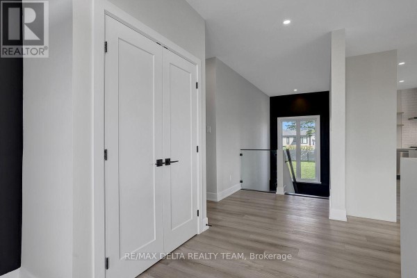 Hallway inside a modern home featuring light wood floors, white double doors, and a view of the staircase. - 1710 Metcalfe Farm Road, Ottawa