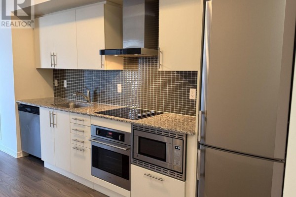 Kitchen with light beige cabinetry, granite countertops, stainless steel appliances, and a mosaic tile backsplash. - 1711 - 352 Front Street W, Toronto