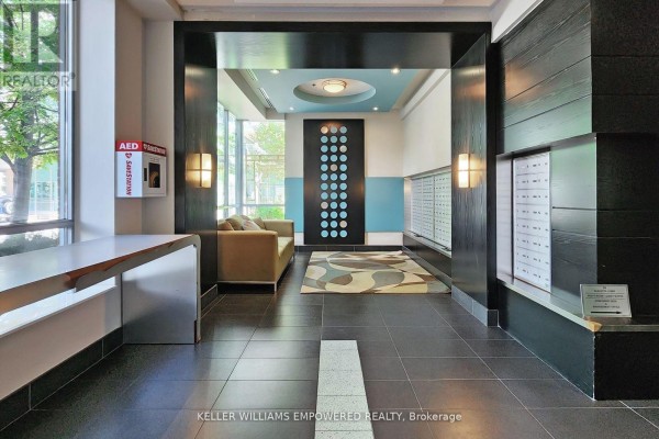 Apartment building lobby with mailboxes, seating area, and decorative wall panels. - 1711 - 50 Lynn Williams Street, Toronto