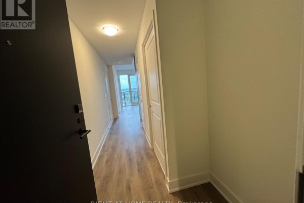 Apartment entryway hallway with dark door, light wood floors, and white doors. - 1711a - 115 Nipissing Road N, Milton