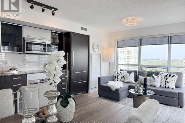 View of kitchen with gray cabinets, dining table, and living area with gray sectional sofa. - 1712 - 5168 Yonge Street, Toronto
