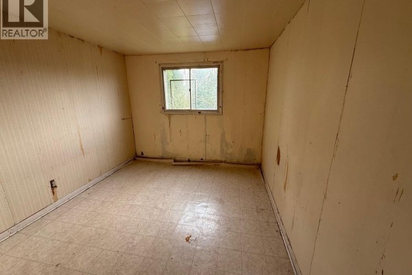 An empty room with beige paneled walls, a linoleum floor, and a single window. - 1712 103rd Street, North Battleford