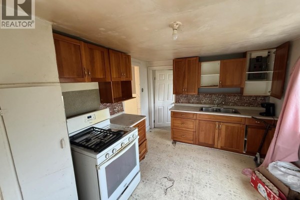 A kitchen with wood cabinets, a white stove, a double sink, and tiled backsplash. - 1712 103rd Street, North Battleford