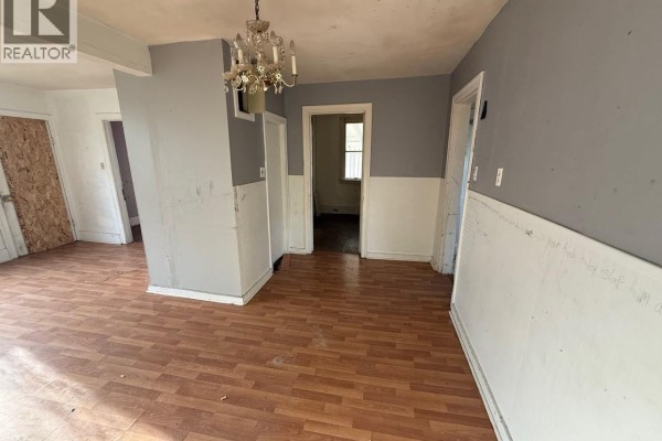 A room with wood-look linoleum flooring, gray and white walls, and an ornate chandelier. - 1712 103rd Street, North Battleford
